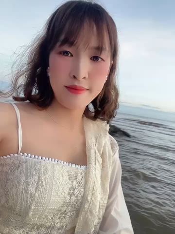 Smiling woman in a white lace top by the sea, seen on a live video chat