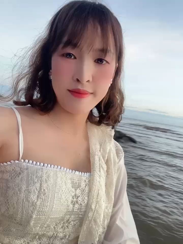 Smiling woman in a white lace top by the sea, seen on a live video chat